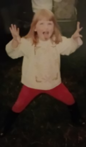 A young girl posing for the camera holding her hands out to the side and sticking her tongue out