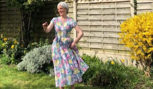 A woman in a floral dress is dancing in her garden on a sunny day