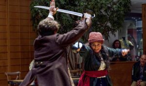 A man and woman in period costume engage in a sword fight