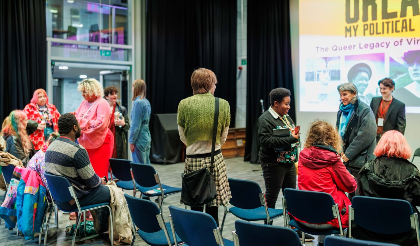 The Courtyard's Nell Gwynne studio filled with attendees, many of which are wearing vibrant pink and blue coloured clothing. 