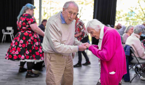 Courtyard Dementia Friendly Tea Party  an older gentleman and lady are dancing together and smiling