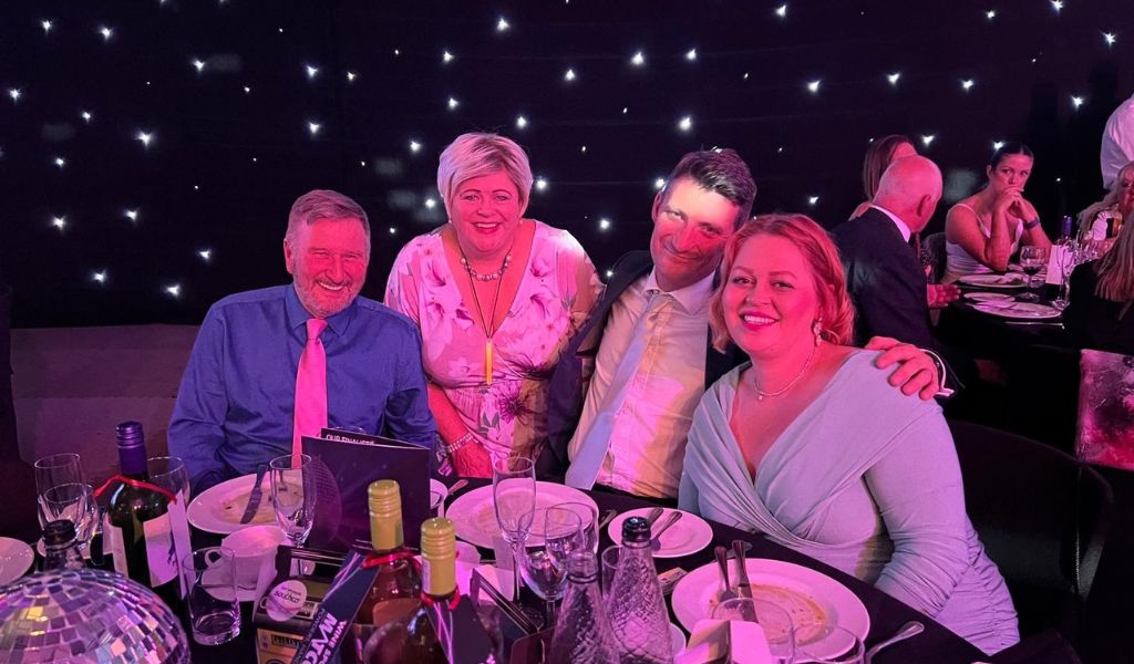 Four people dressed smartly sat smiling at a table.