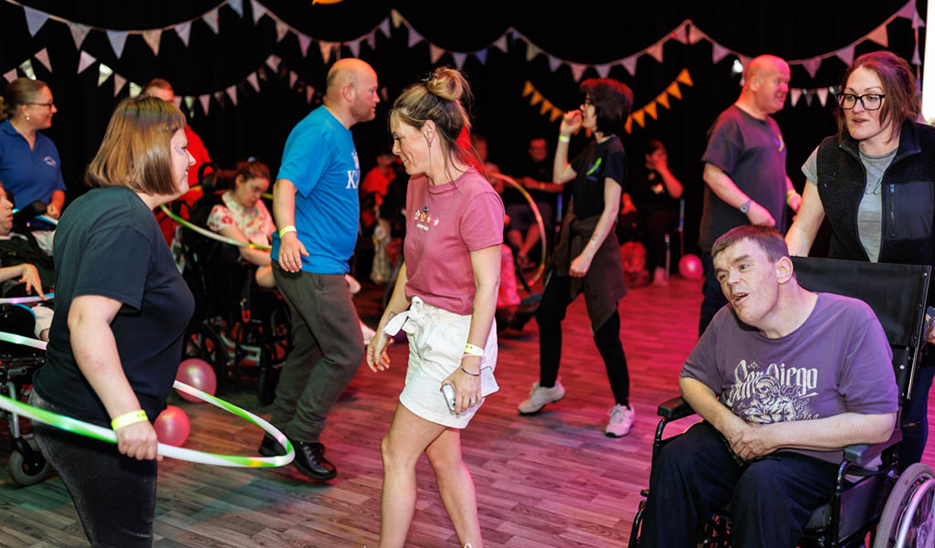 Joy Club – Inclusive Adult Rave: Several people, some in wheelchairs, dance in a studio space, they're surrounded by bunting and balloons.
