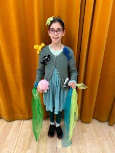 A young girl dressed up with sea creatures stuck to her and green scarves handing from her hands.