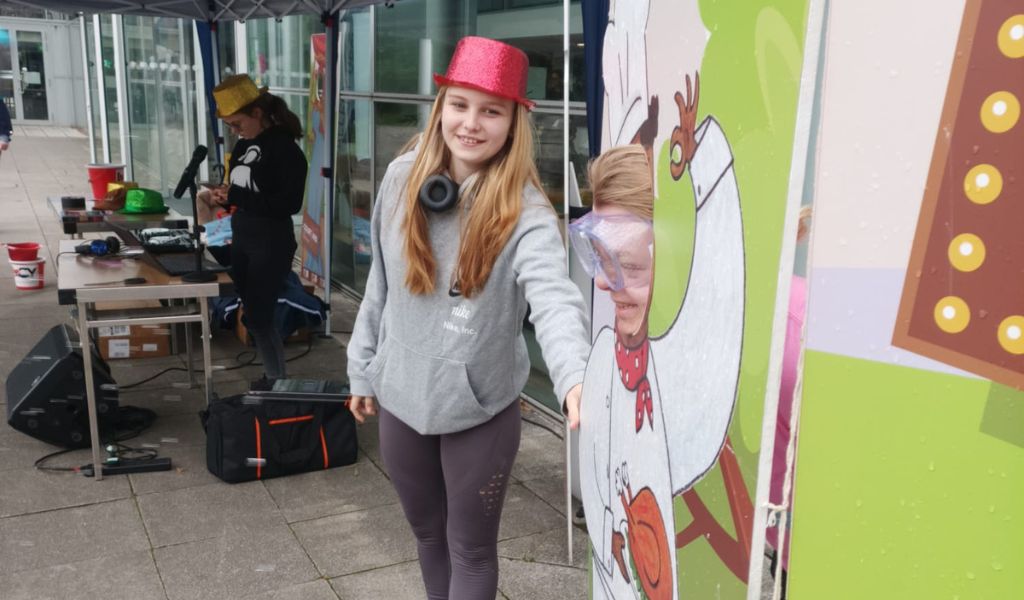 Two young girls pose next to a cardboard cut out. One wears gogles.
