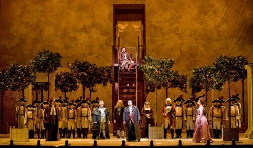 A large stage performance feature an ensemble cast trees and a staircase