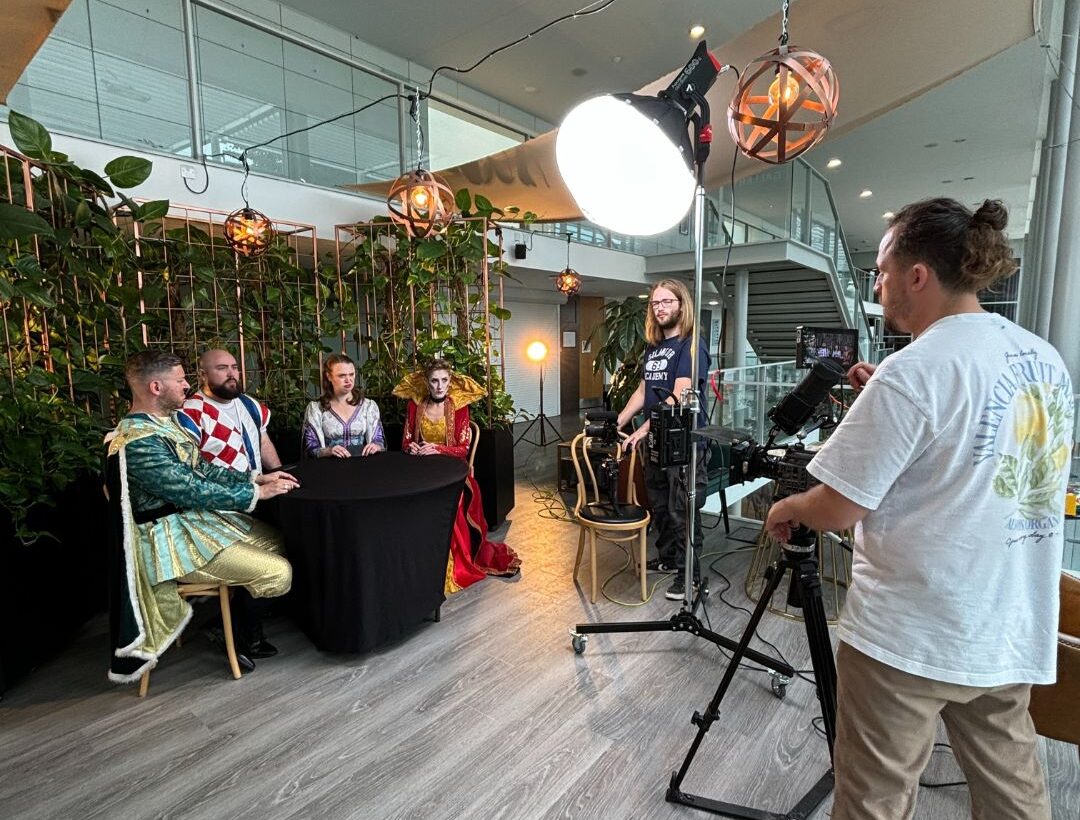 A film maker filming four characters sat around a table.