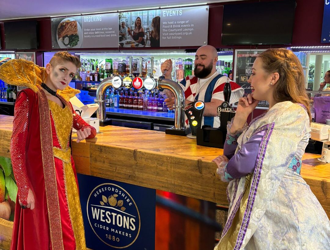 Two pantomime characters lean against The Courtyard bar, another pulls a pint.