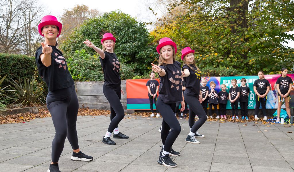A group of women dance on The Courtyard patio in pink sparkly hats