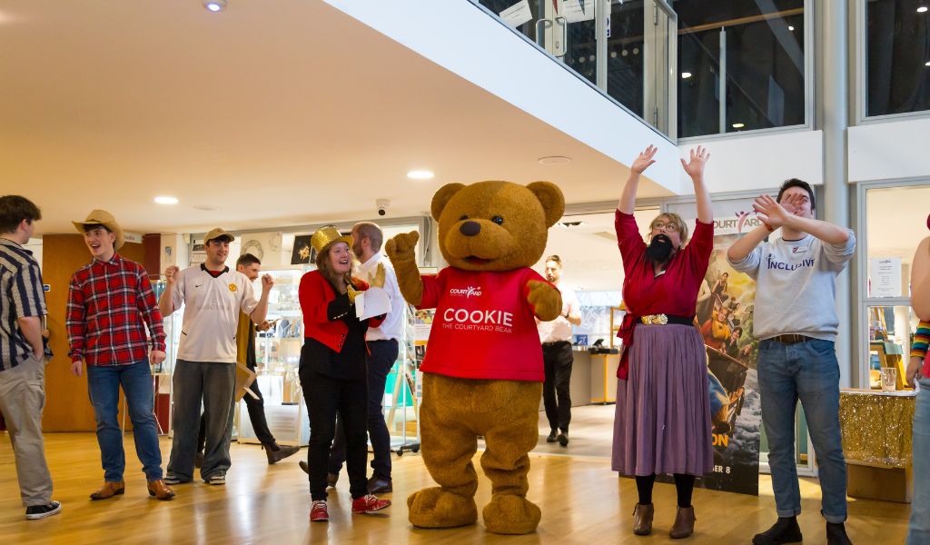 A group of people in costume sing in The Courtyard foyer.