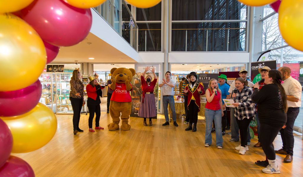 A group of people in costume sing in The Courtyard foyer.