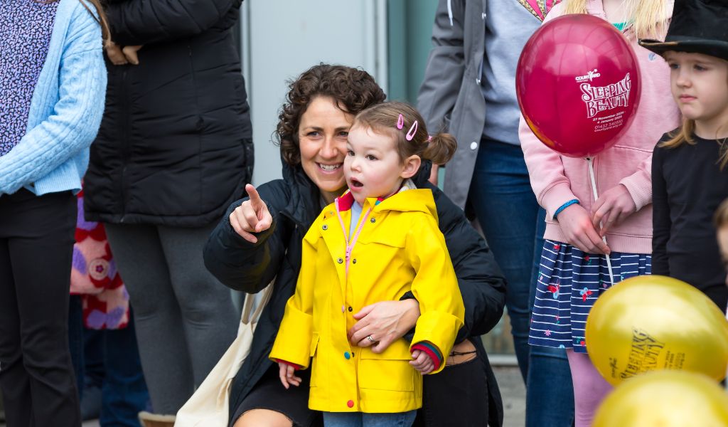 A young girl stands looking shocked while an adult points at something