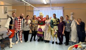 Five members of the pantomime cast in costume posing for a photo with staff members from Hereford Hospital Children's Ward