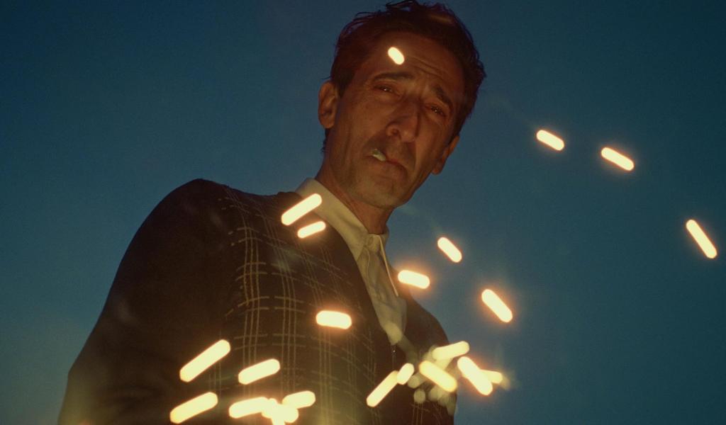 A man smokes a cigarette as the embers of a fire flicker in front of his face. 