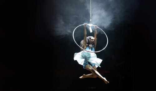 NoFit State perform SABOTAGE  a woman in a tutu hangs from a hoop int he sky