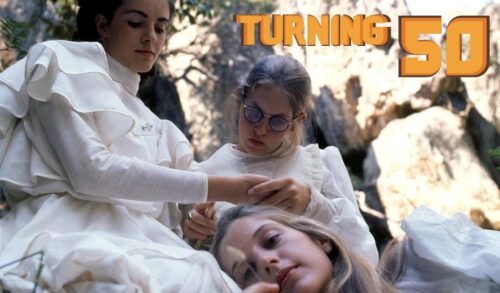 Three girls in white dresses rest on each other outside in front of a large rock In the top right the text reads Turning 50