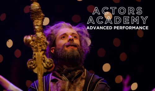 Actors Academy Advanced Performance  A young performer wears a costume including a bushy beard they are looking into the distance holding an elaborately decorated gold staff
