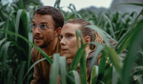 A man and a woman crouch in tall grass