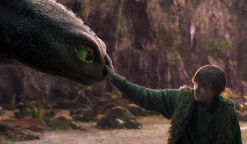A young boy places his hand on the nose of a large black dragon