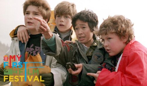A group of four young boys stand pointing in a direction as they hold up an old treasure map and a compass