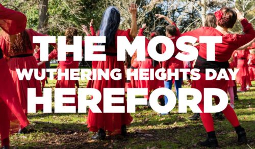 The Most Wuthering Heights Day  Hereford Text in front of a a group of people in red dresses dancing in a field
