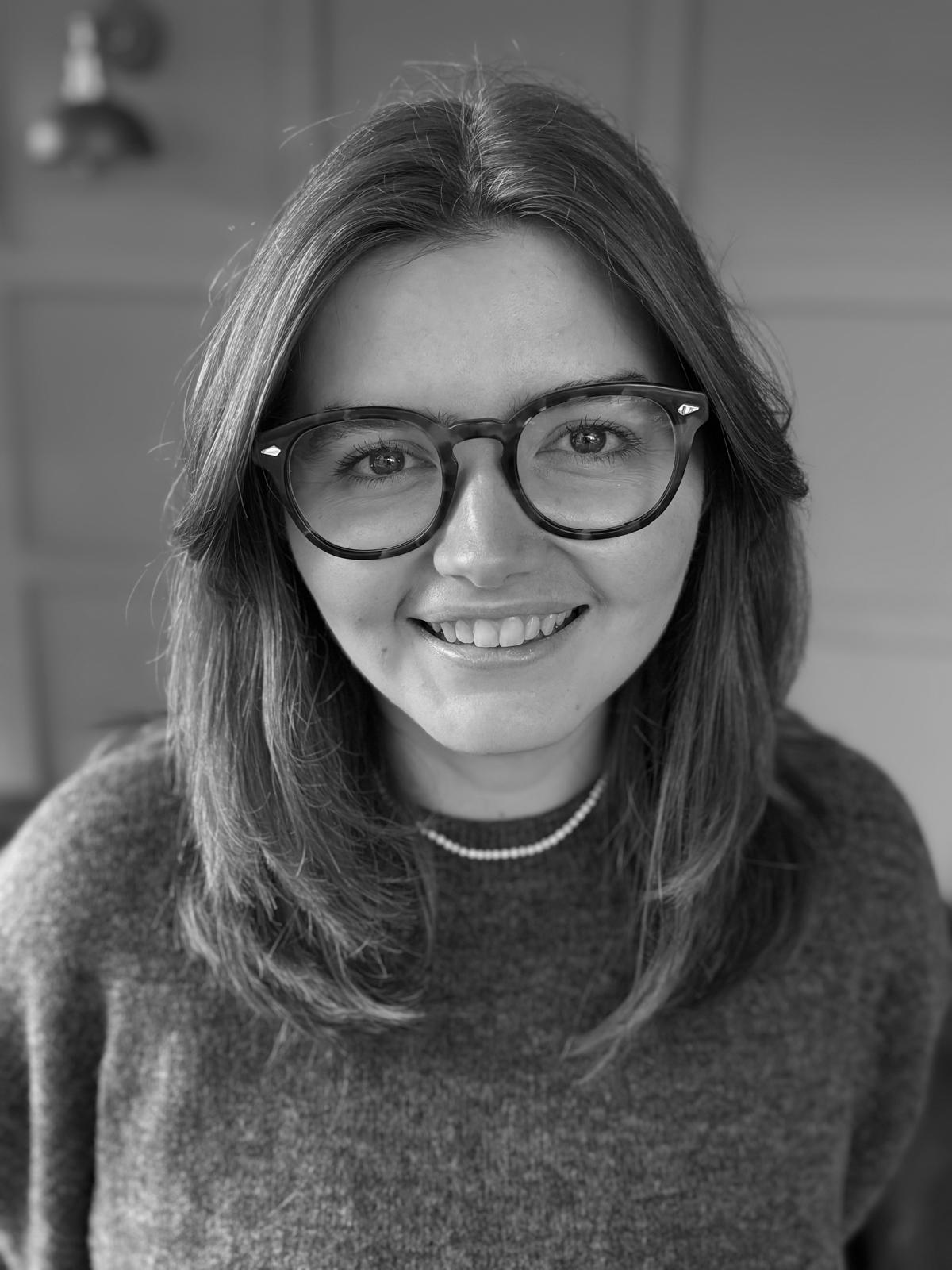 A photo of a woman wearing glasses and a jumper smiling.