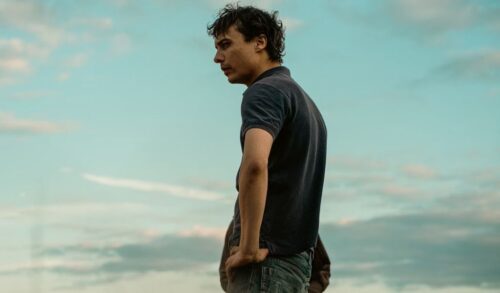 A man stands with his hands on his hips Behind him is a blue sky