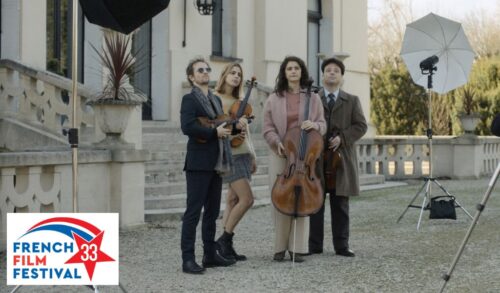 A quartet of musicians stand holding cellos and violins outside a stately home Around them are large photography lights In the bottom left is the French Film Festival UK logo