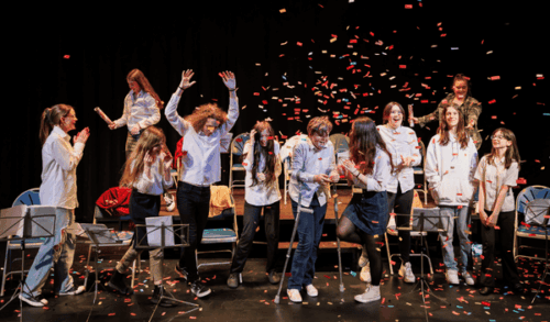 A group of children celebrating on stage with confetti going around them