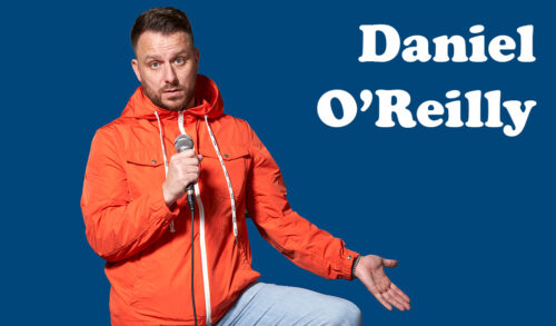 A man in an orange rain coat holding a microphone and holding his other hand out The text to his right reads Daniel OReilly