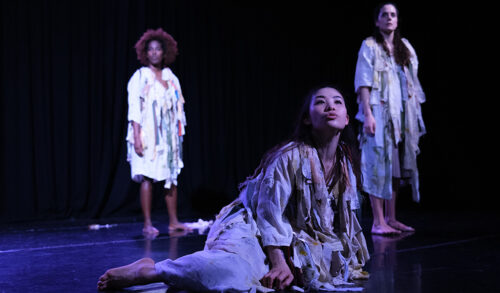 Three dancers on stage in white outfits looking up