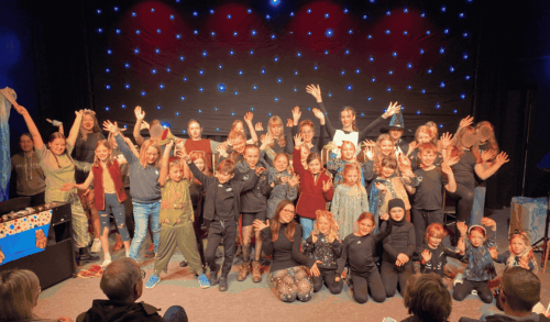 A group of children on stage with their hands in the air