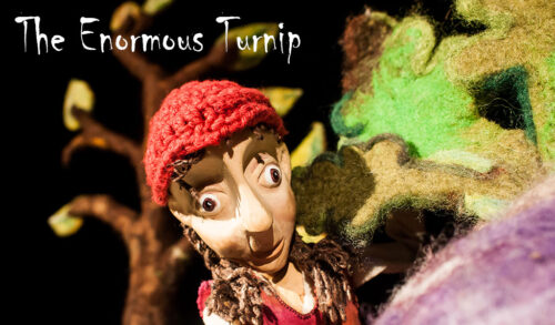 A puppet with a red hat stood next to the felt leaves of a felt turnip The text above reads The Enormous Turnip