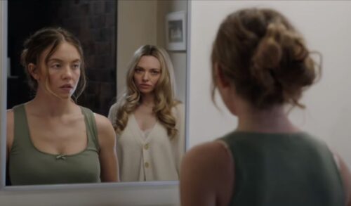 Two women stood next to each other look into a mirror that they are reflected in