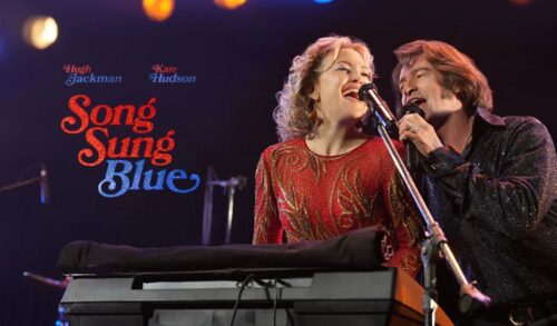 A man and a woman perform on stage behind a keyboard and a microphone Both are wearing bedazzled outfits The title reads Song Sung Blue