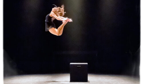 A woman in a black leotard jumping midair off of a black box