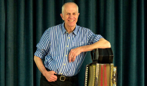 An older man in a blue and white striped shirt leaning against an accordion