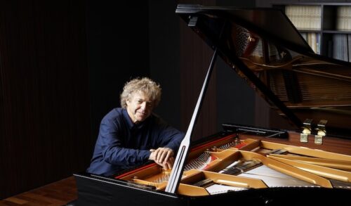 A man in a dark blue shirt sitting at a piano and smiling