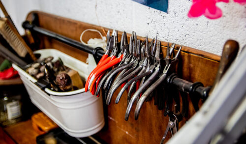 A photo of metal pliers hanging on a rail with a bucket of other metal tools behind it