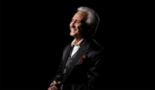 A photo of an older gentleman in a black formal suit smiling and looking off to the left of the image