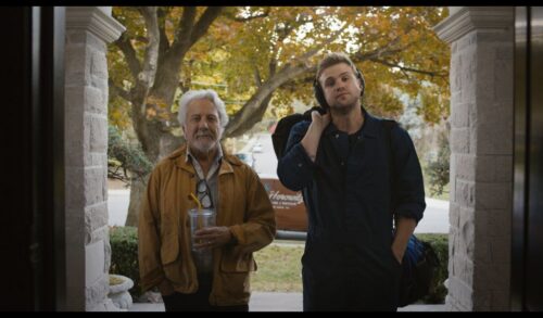 A young man and old man stood in the doorway of a house looking at the camera