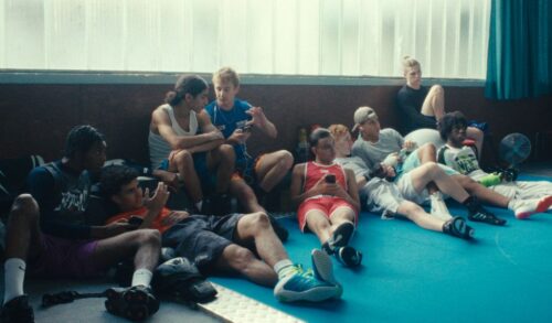A group of teenagers sitting and leaning against a wall with a window behind them