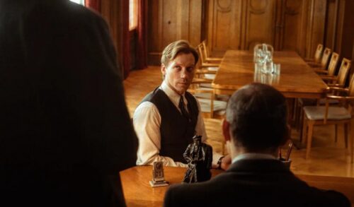 A lawyer in waistcoat sits across from two people in black suits